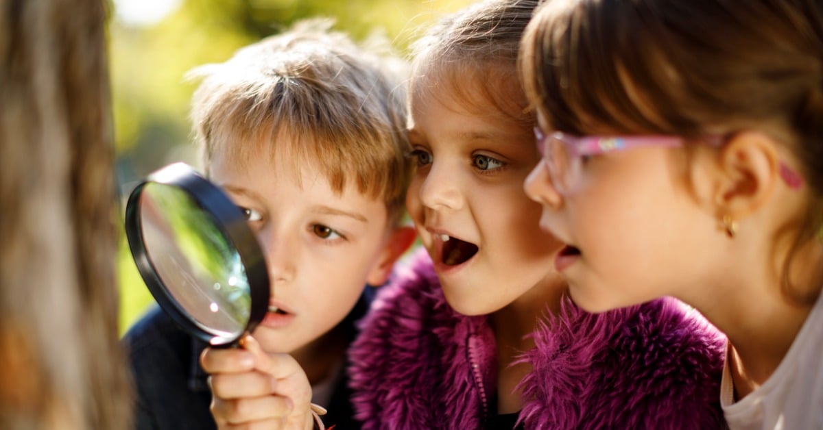 Three children looking through a magnifying glass examining something up close.
